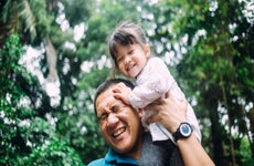 Asian father carries his daughter on his shoulders while they spend some time outside.