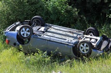 A shot of a gray car flipped over on its roof off the road after an accident.