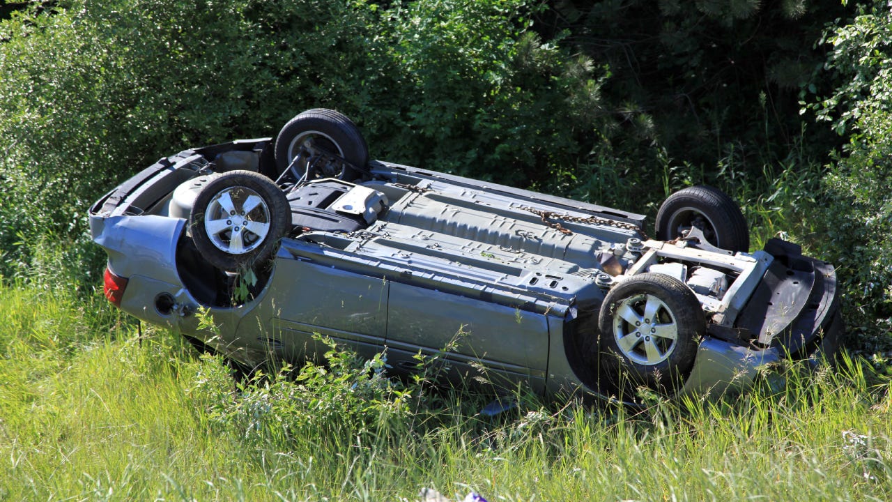 A shot of a gray car flipped over on its roof off the road after an accident.