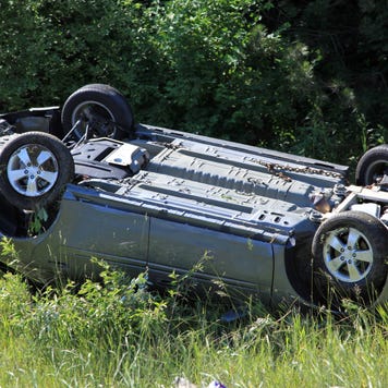 A shot of a gray car flipped over on its roof off the road after an accident.