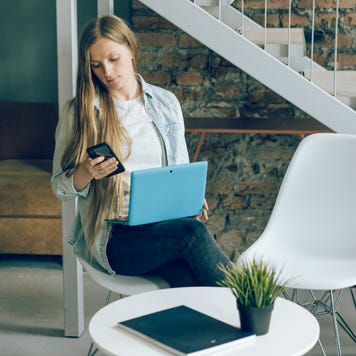 A lady uses her phone and laptop.