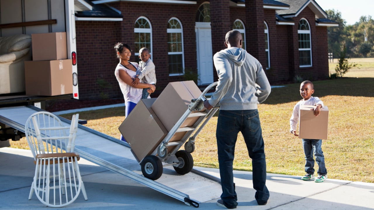 A Black family unloading a moving truck at a house in the suburbs.