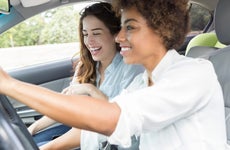 Two young ladies, one black and one white, driving and having fun in the car laughing.