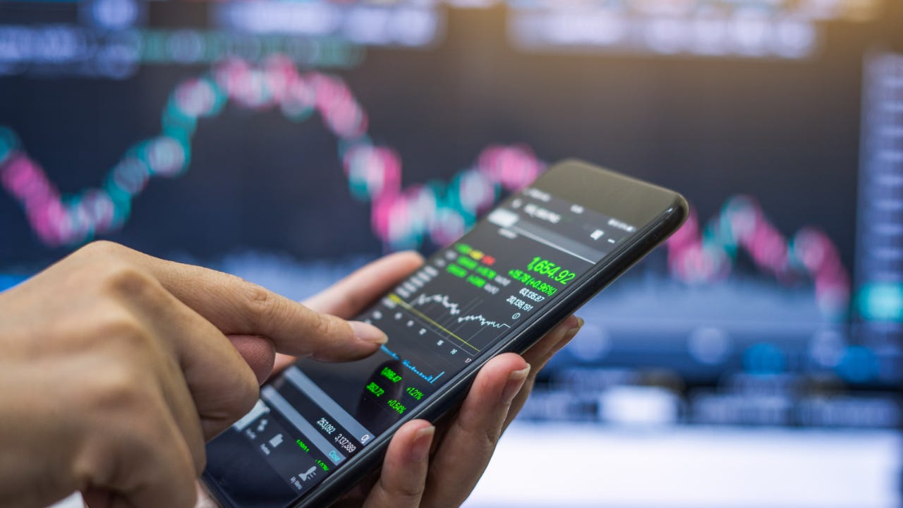 A trader holds a phone with a stock chart on it