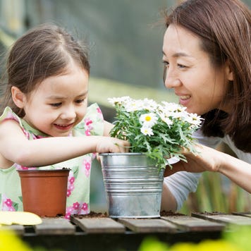 Mixed-race Asian girl and her Asian mother are potting a plant and enjoying the weather outdoors.