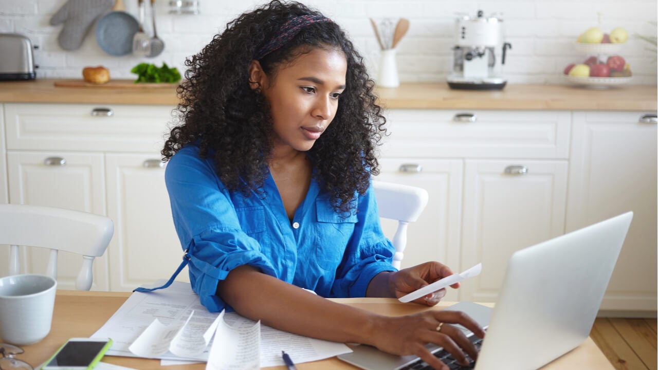 Indoor shot of attractive serious young dark skinned with wavy hair doing paperwork in kitchen
