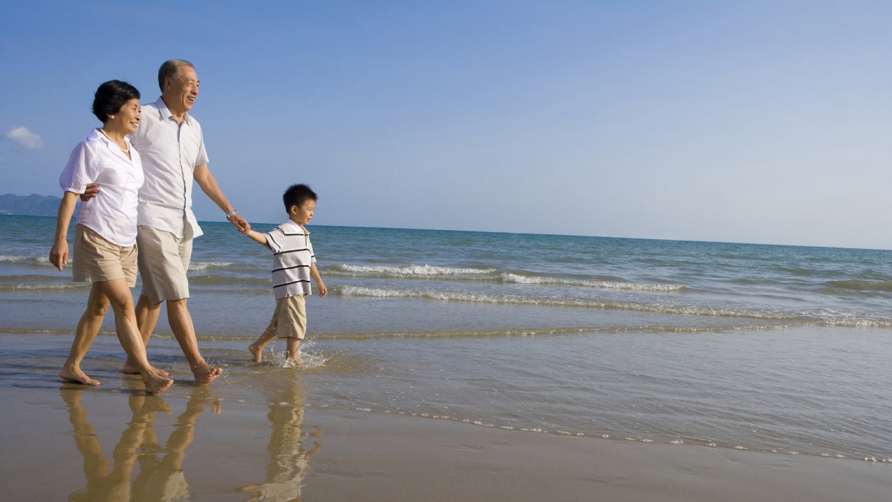 A senior couple of Asians are walking along the beach on a sunny day with their grandson.