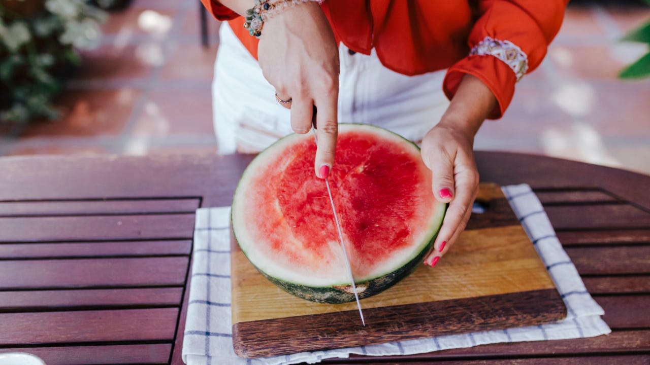 A woman cuts a watermelon in half