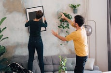 Mid adult man guiding girlfriend in hanging picture frame on wall at new home