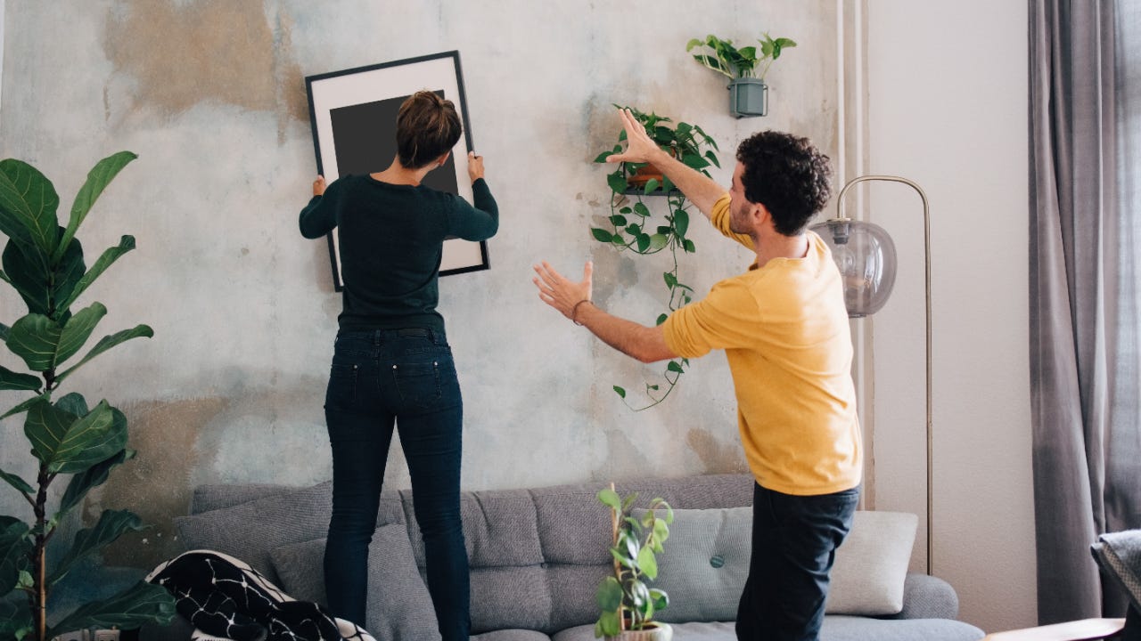 Mid adult man guiding girlfriend in hanging picture frame on wall at new home