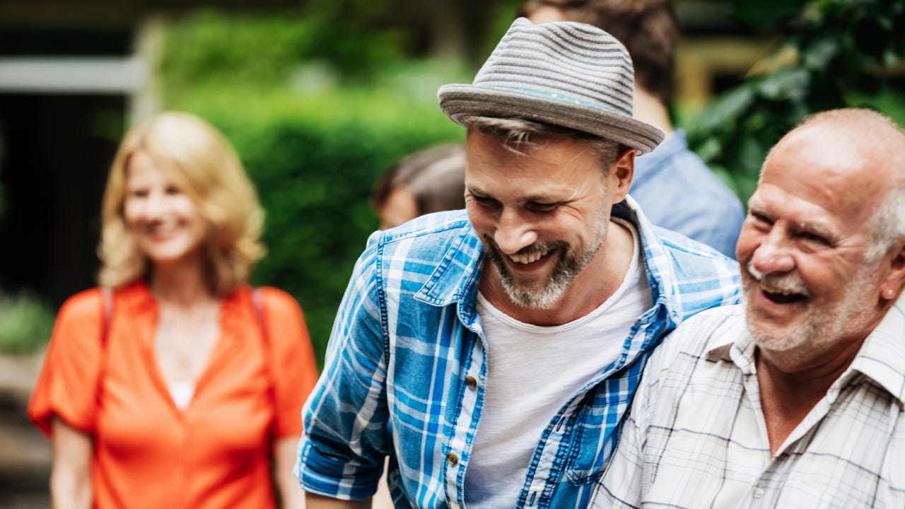 An adult son is spending time with his father out in the backyard during a family cookout.