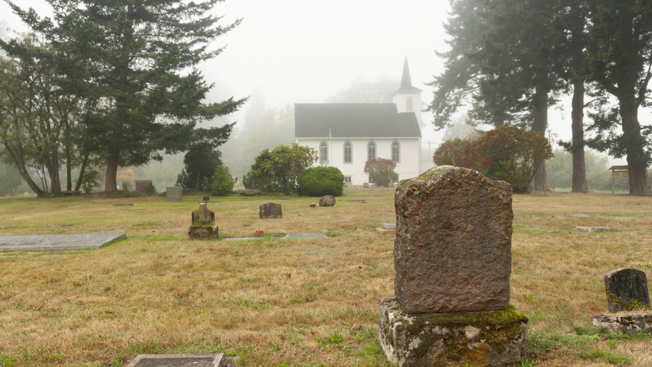 A scenic cemetery outside of an old chapel on a foggy day.