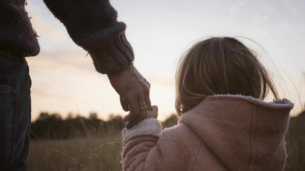 A granddaughter holding her grandpa's hand and staring at the sunset.