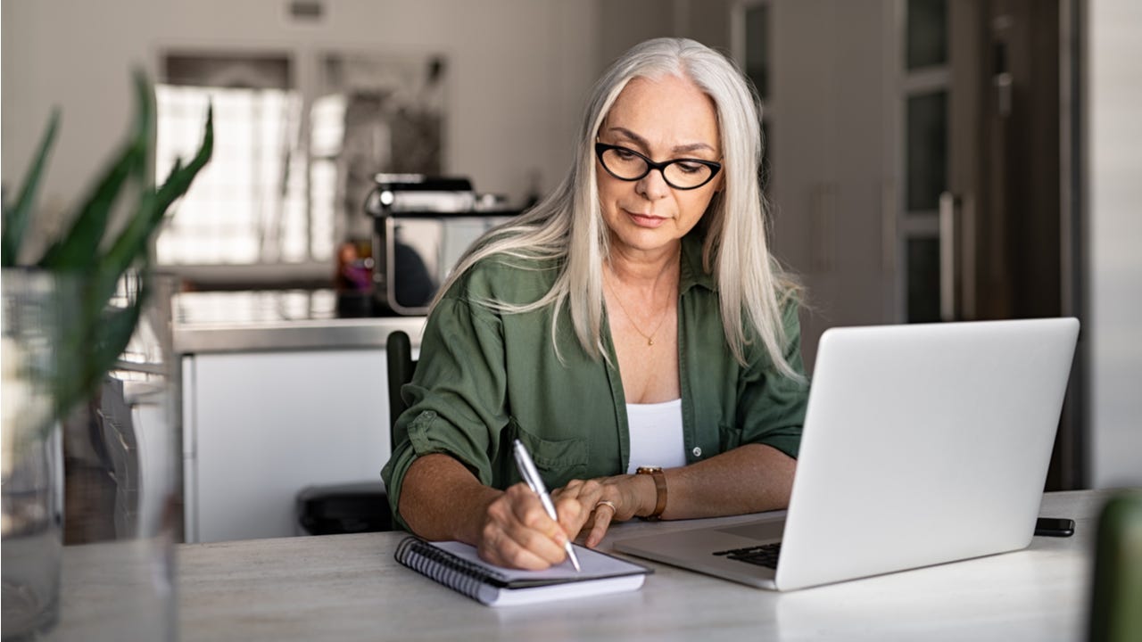 Woman writes in a notebook while working on a laptop