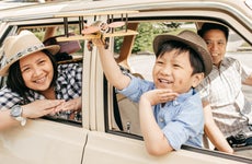 An Asian family going for a drive with the son in the passenger seat holding a toy airplane out the window. (The car is parked).