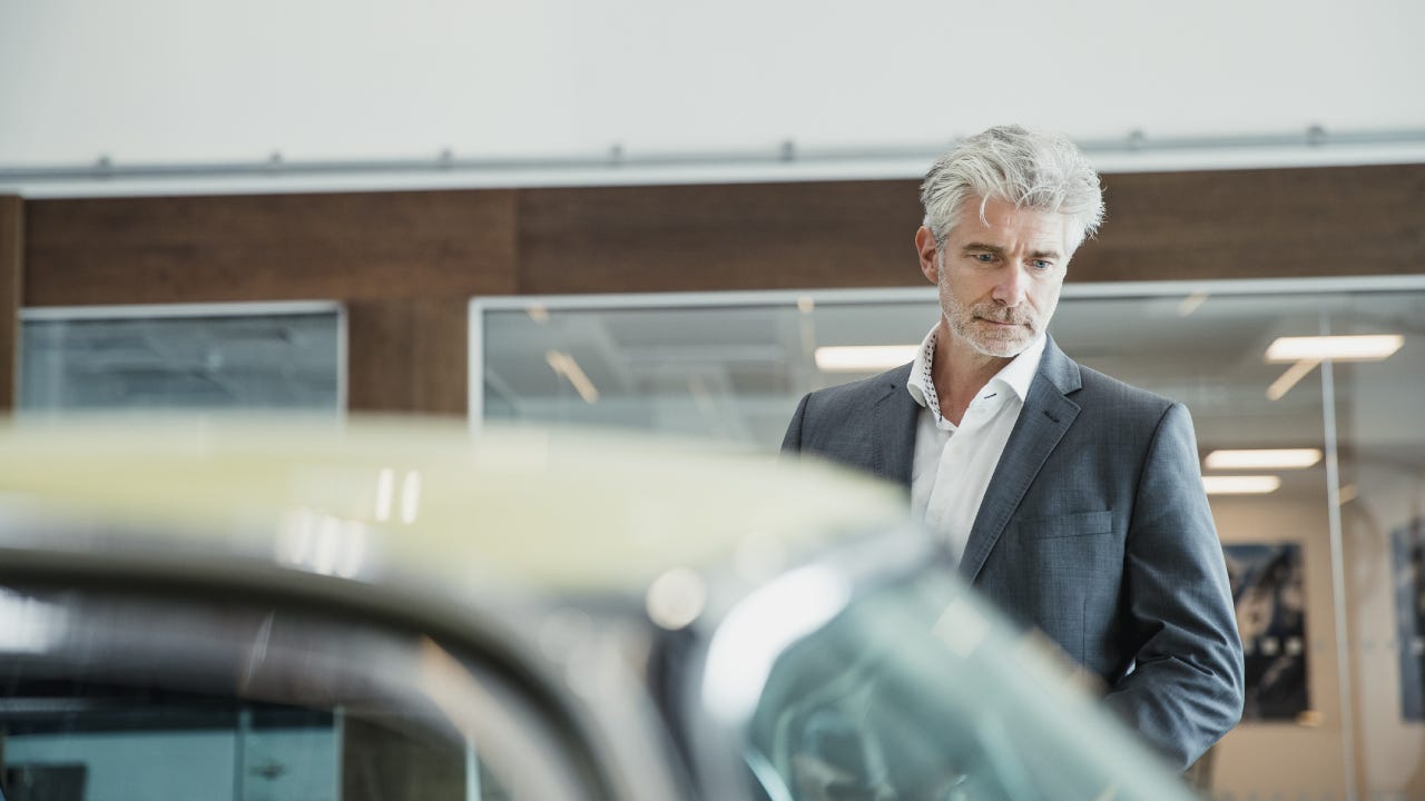 An older gentleman stands in a showroom looking at a car.