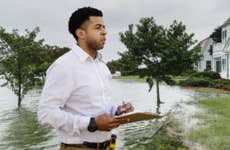 An African-American insurance rep is standing outside of a home in the aftermath of a flood.
