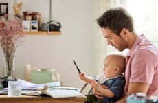 A White father holds his infant son in front of a computer