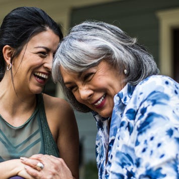 Adult daughter sits with her mother on the porch and are laughing together.