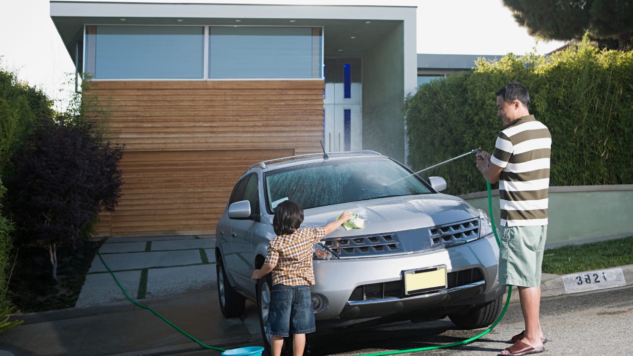 A father and child washing their car in the driveway.