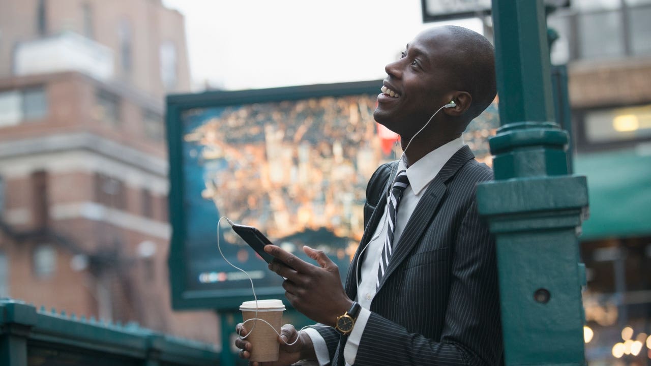 A black businessman in New York City listens to a podcast while walking