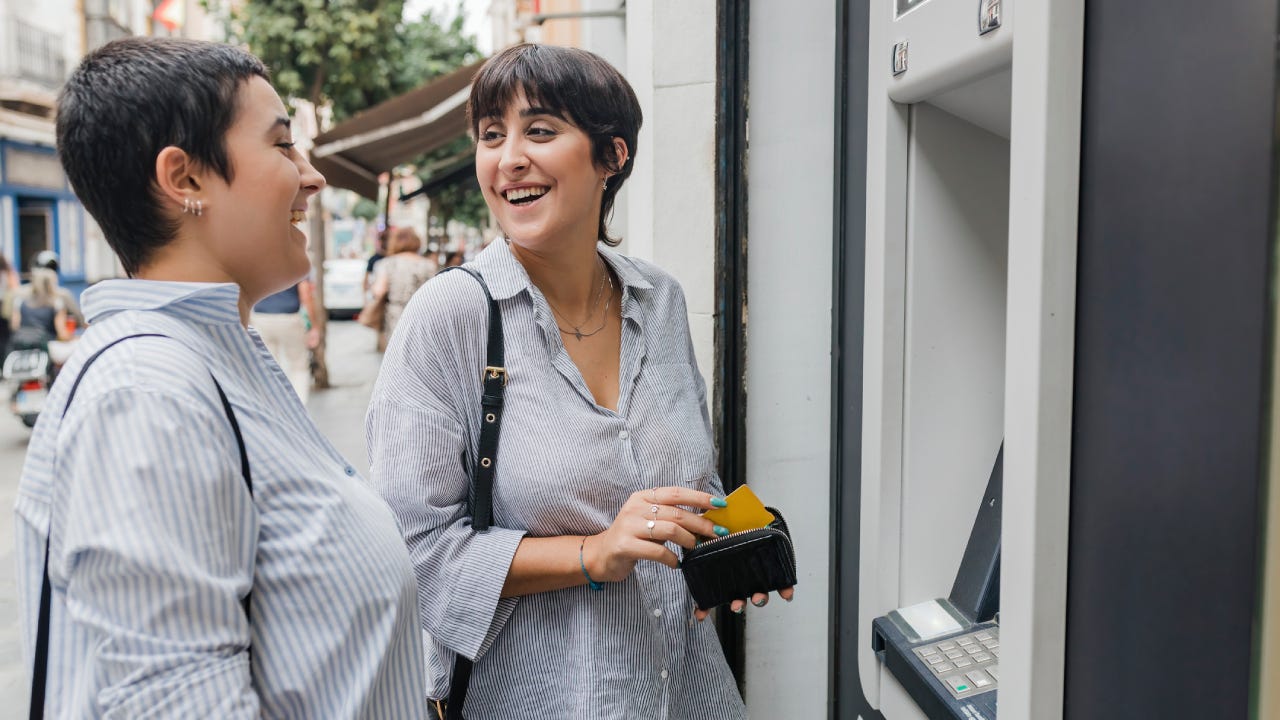 Happy women talking to each other standing near ATM machine