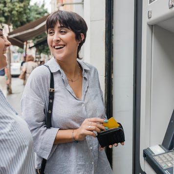 Happy women talking to each other standing near ATM machine
