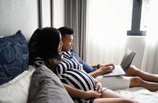 pregnant couple laying down and looking at a laptop