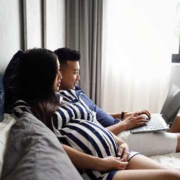 pregnant couple laying down and looking at a laptop