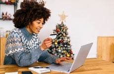 Happy young woman with credit card using laptop sitting at table in living room