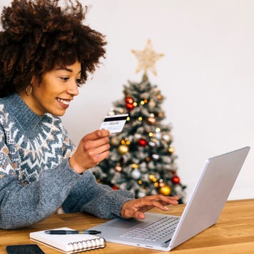 Happy young woman with credit card using laptop sitting at table in living room