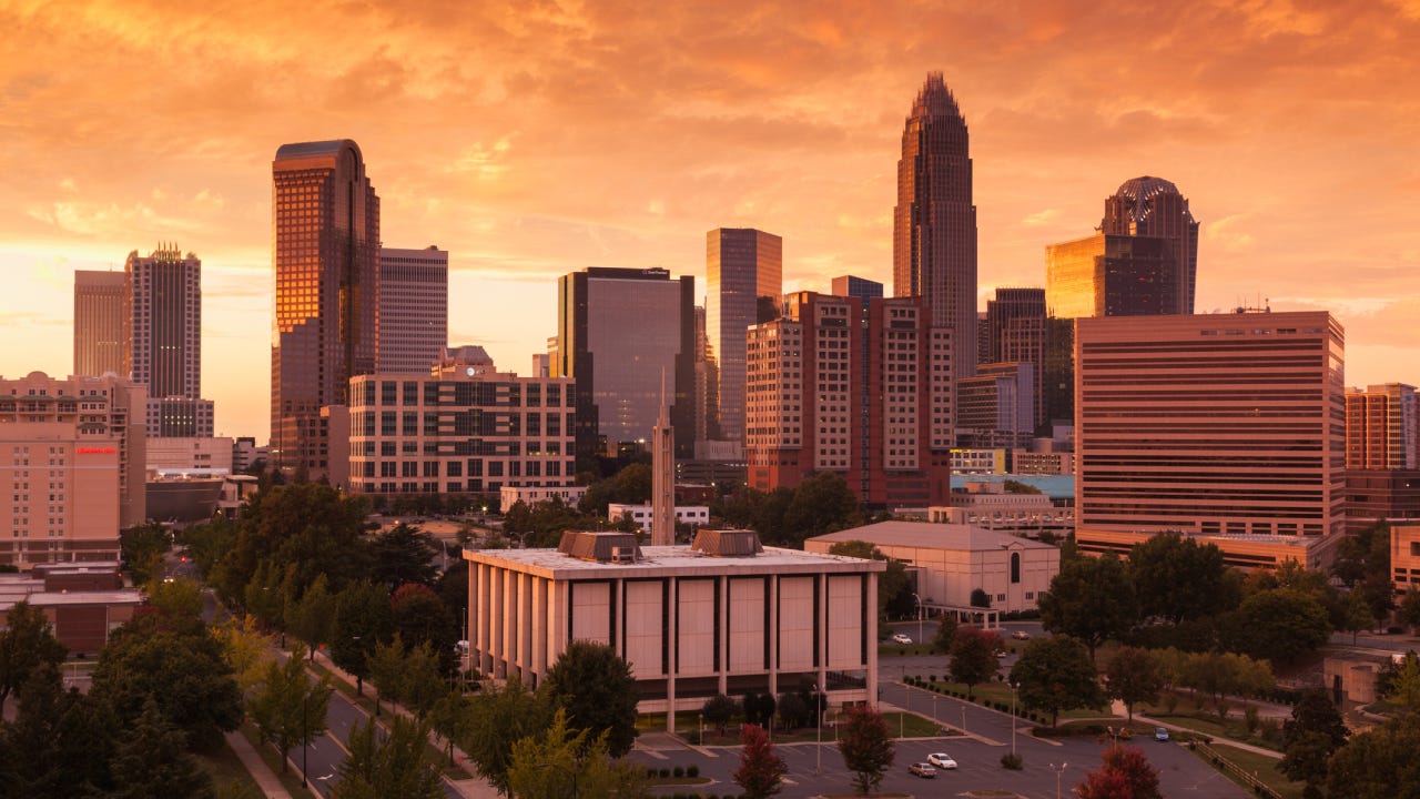 Skyline of Charlotte, North Carolina against the orange sky of a setting sun.