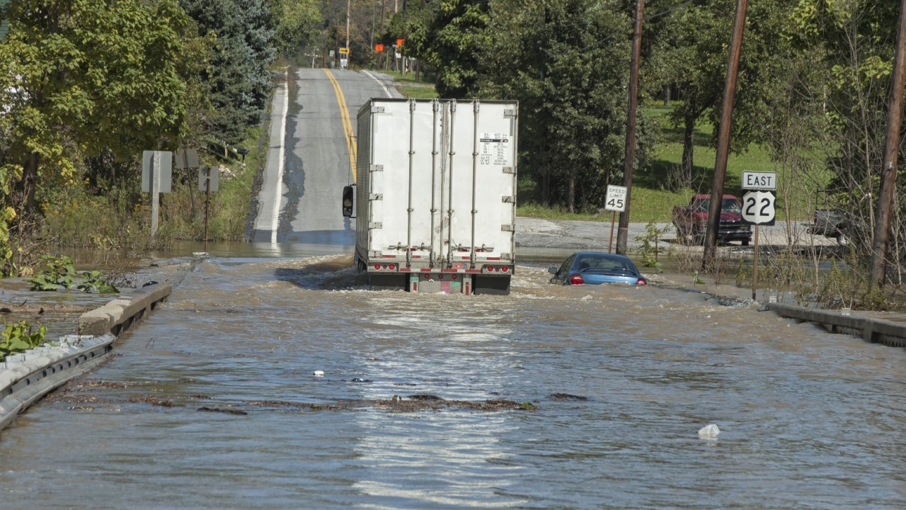 An 18-wheeler and a small blue car half-submerged in a flooded roadway.