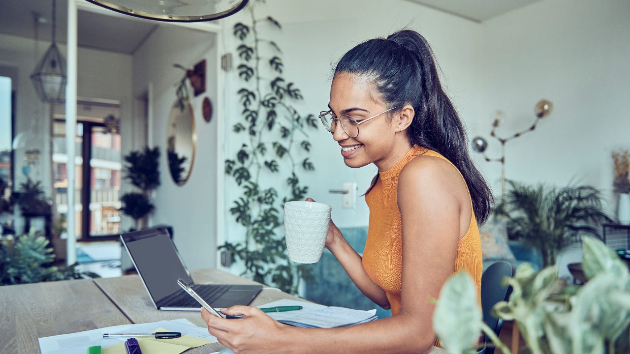 A young woman checks her phone while at her desk at home