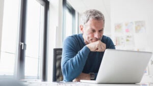 An older White man sits at a laptop computer on his desk