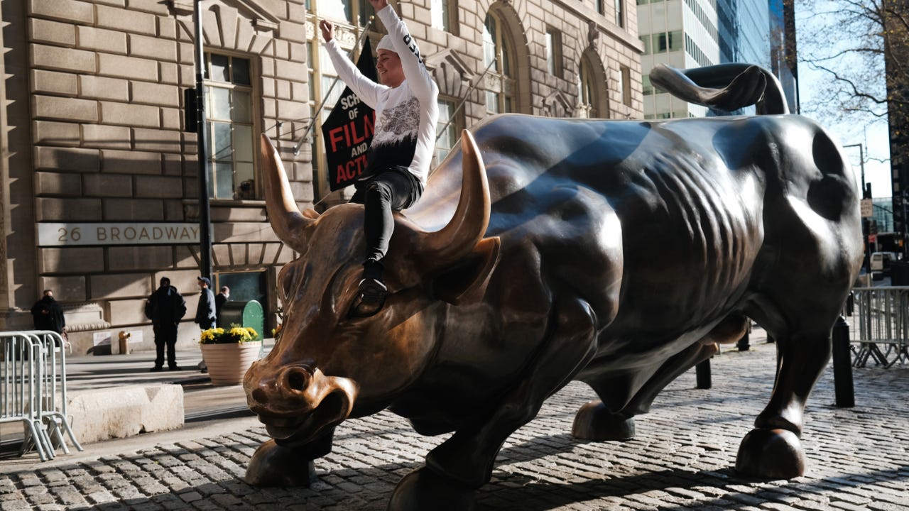A man sits astride the bull in front of the New York Stock Exchange