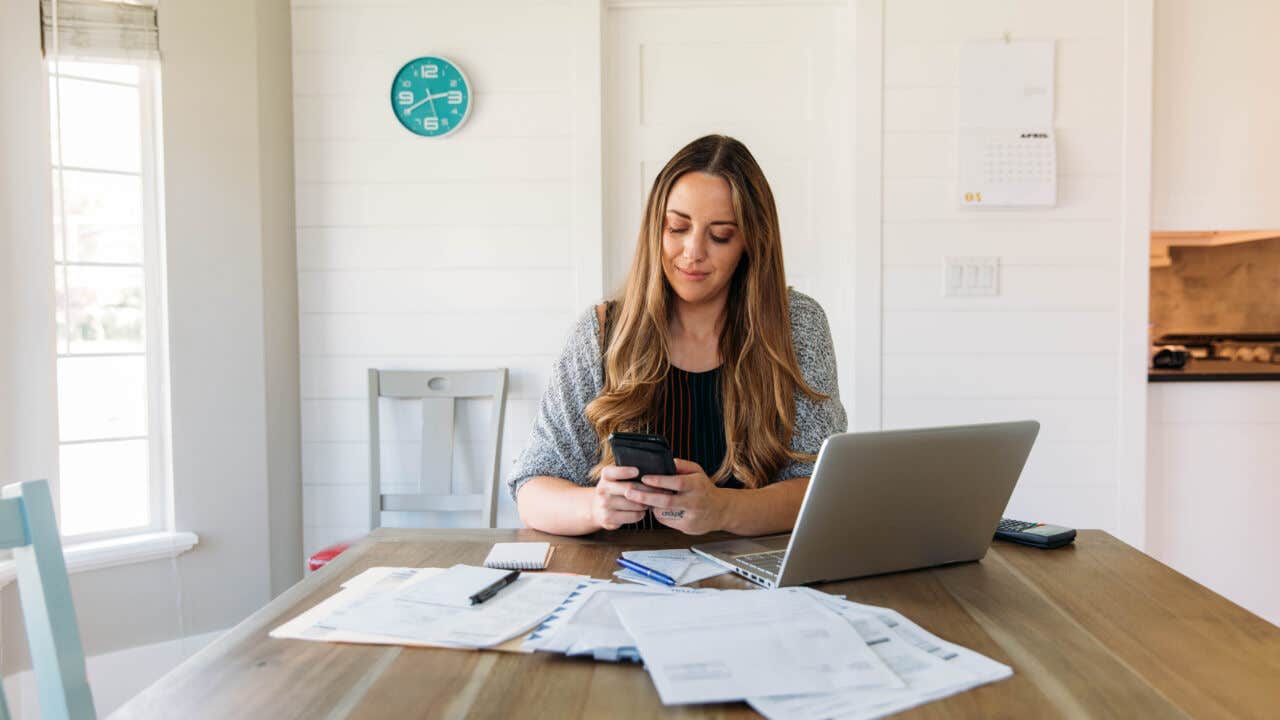 a women on her phone sitting at a table as she presumably goes through her account