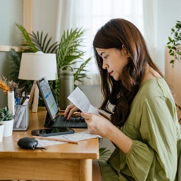 woman looking at paperwork and working on a laptop