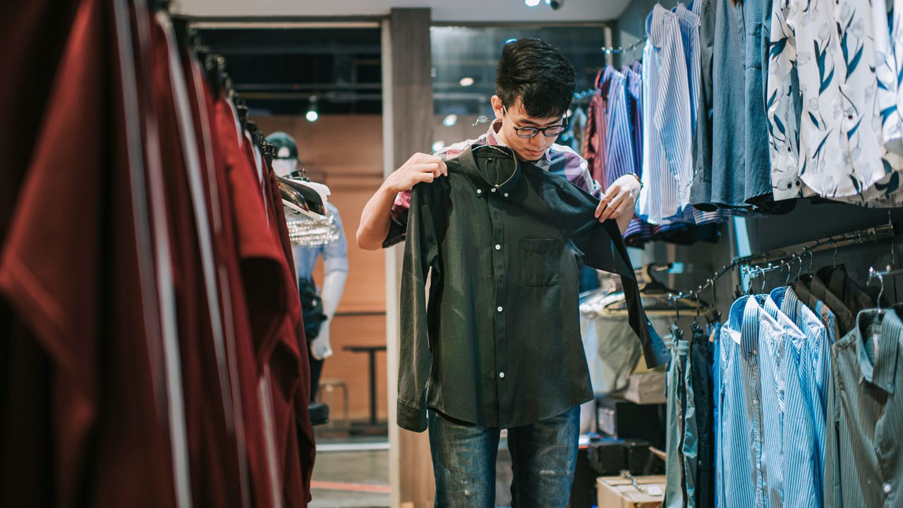 young person holding up a shirt while shopping in a store