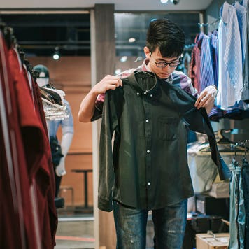 young person holding up a shirt while shopping in a store