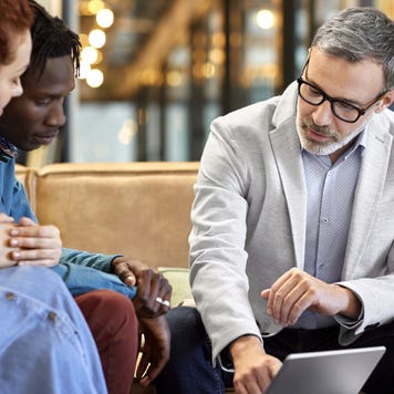 Interracial couple sits on a couch across from a financial expert to review a policy.