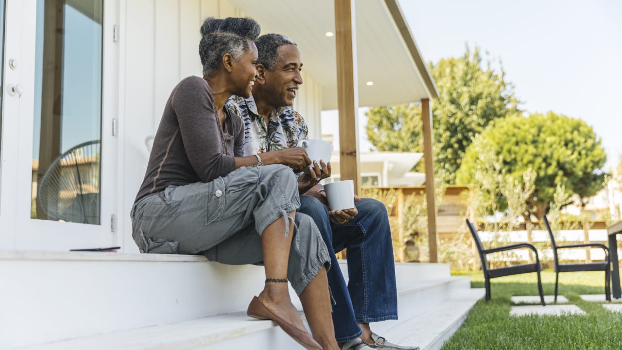 Older black couple sitting on the porch steps of their home with coffee, enjoying the day.