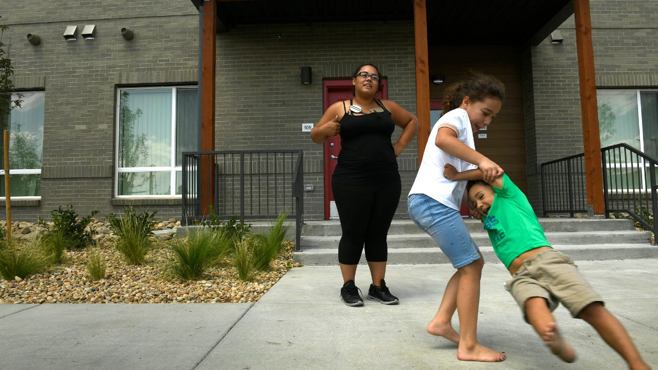Alexandra Loya, 8, horses around with her brother Andrew, 3, while their mother T'nia, in back, watches in front of their new Section 8-subsidized home at the Village at Westerly Creek on July 30, 2018, in Aurora, Colorado.