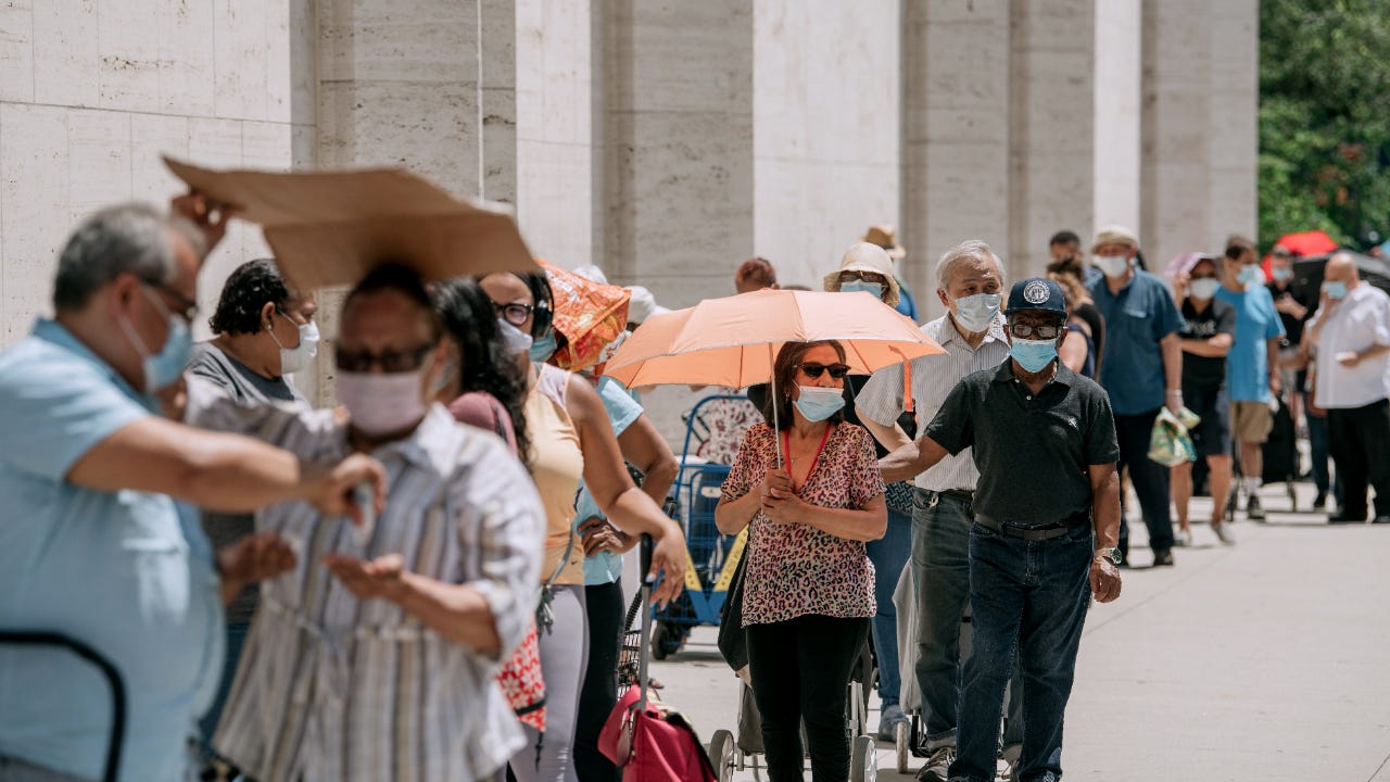 A line of people waits on food handouts in the sun