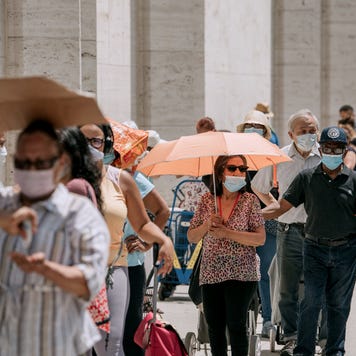 A line of people waits on food handouts in the sun