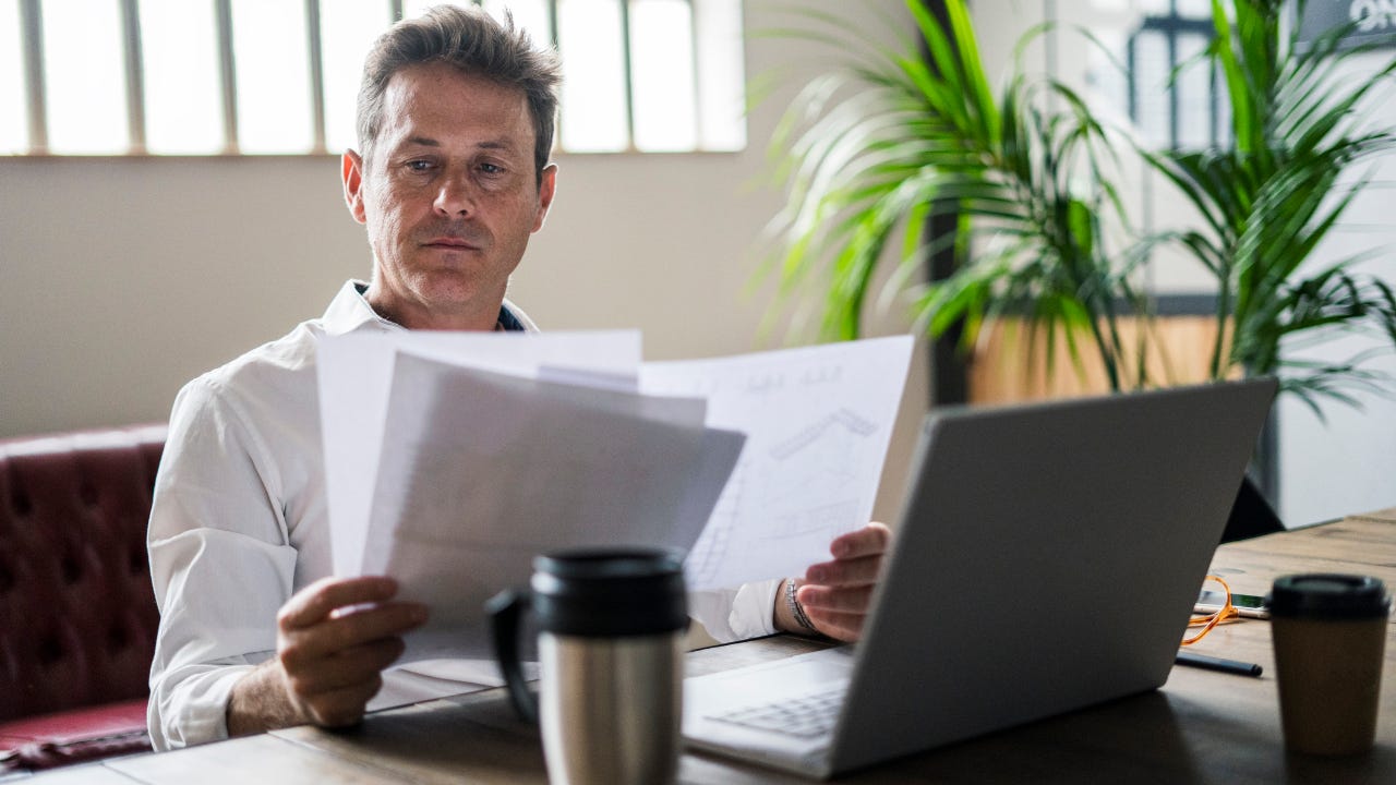 Focused businessman using laptop and reviewing documents at desk