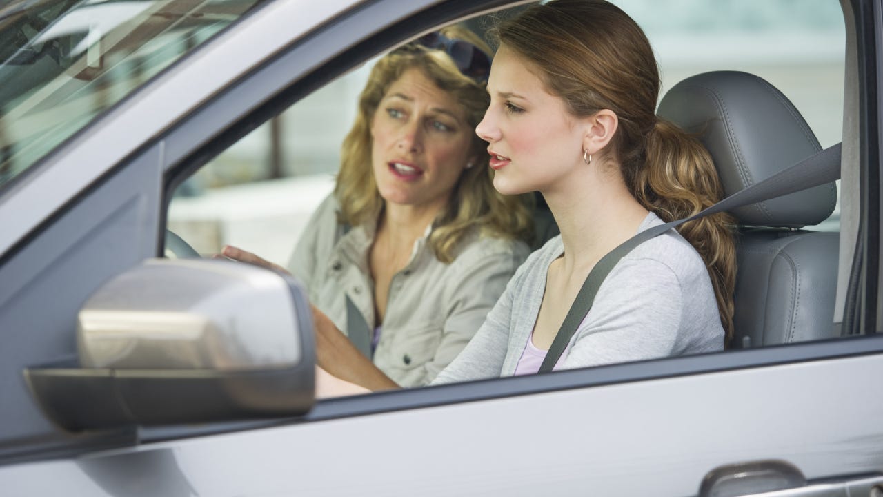 A mother in the passenger seat of her car instructing her daughter who is driving.