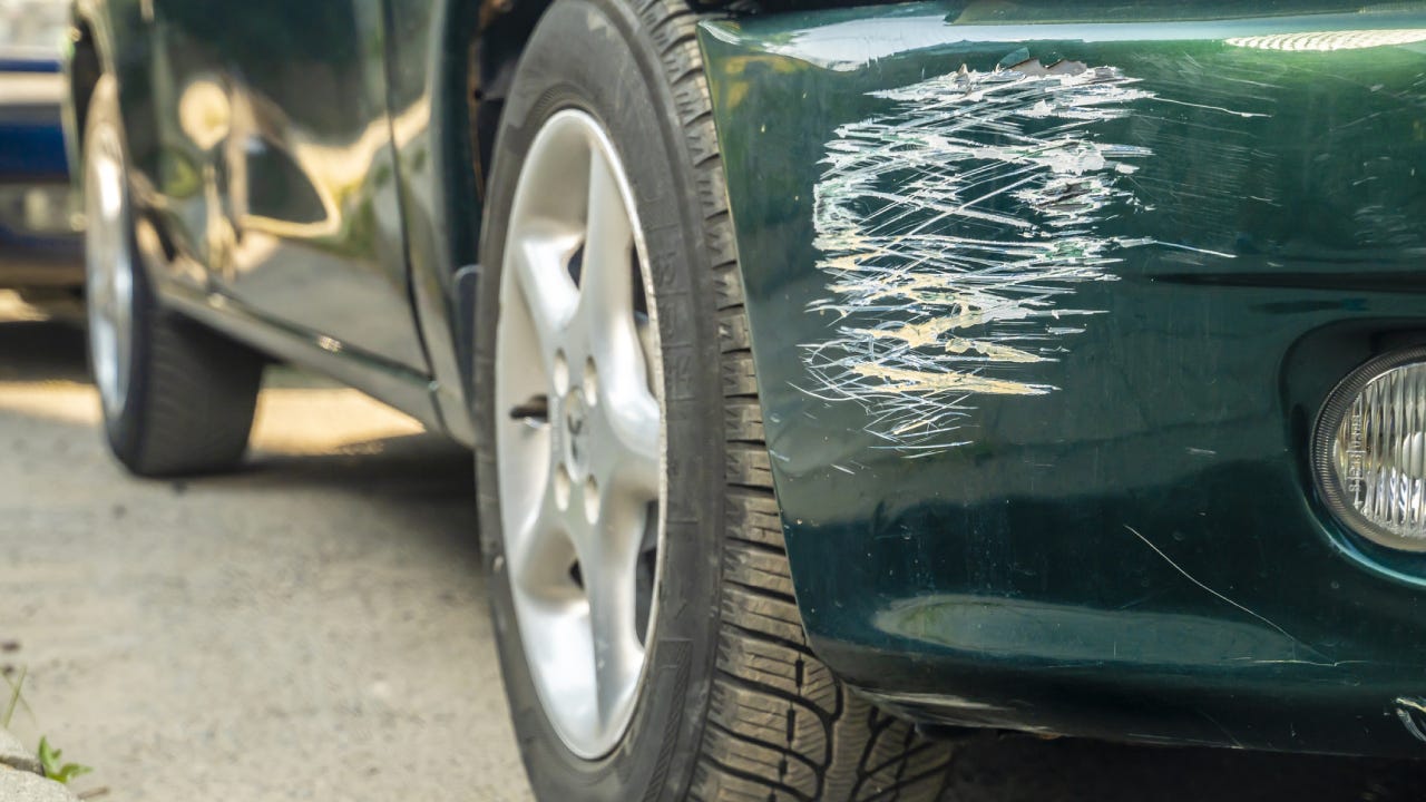 Close-up of a green car with a scratched fender where a white car hit it.