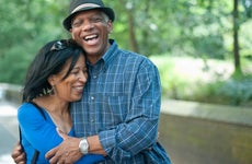A middle-aged Black couple holds one another laughing in front of a park