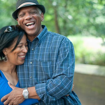 A middle-aged Black couple holds one another laughing in front of a park